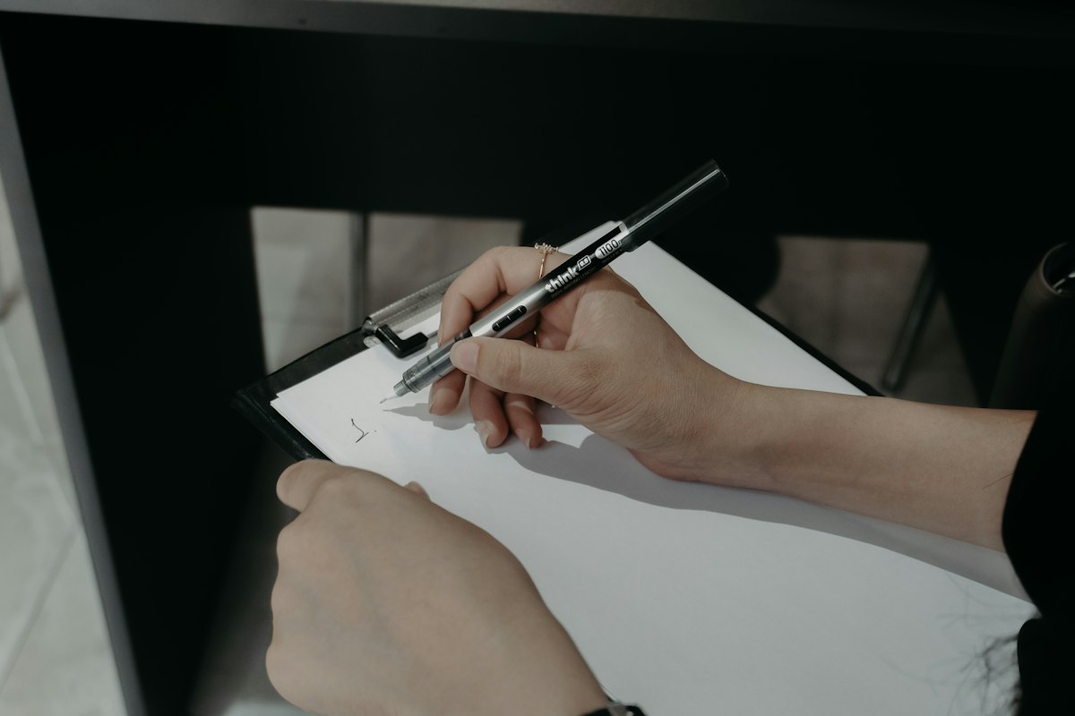 A hand signing off on a clipboard with a pen